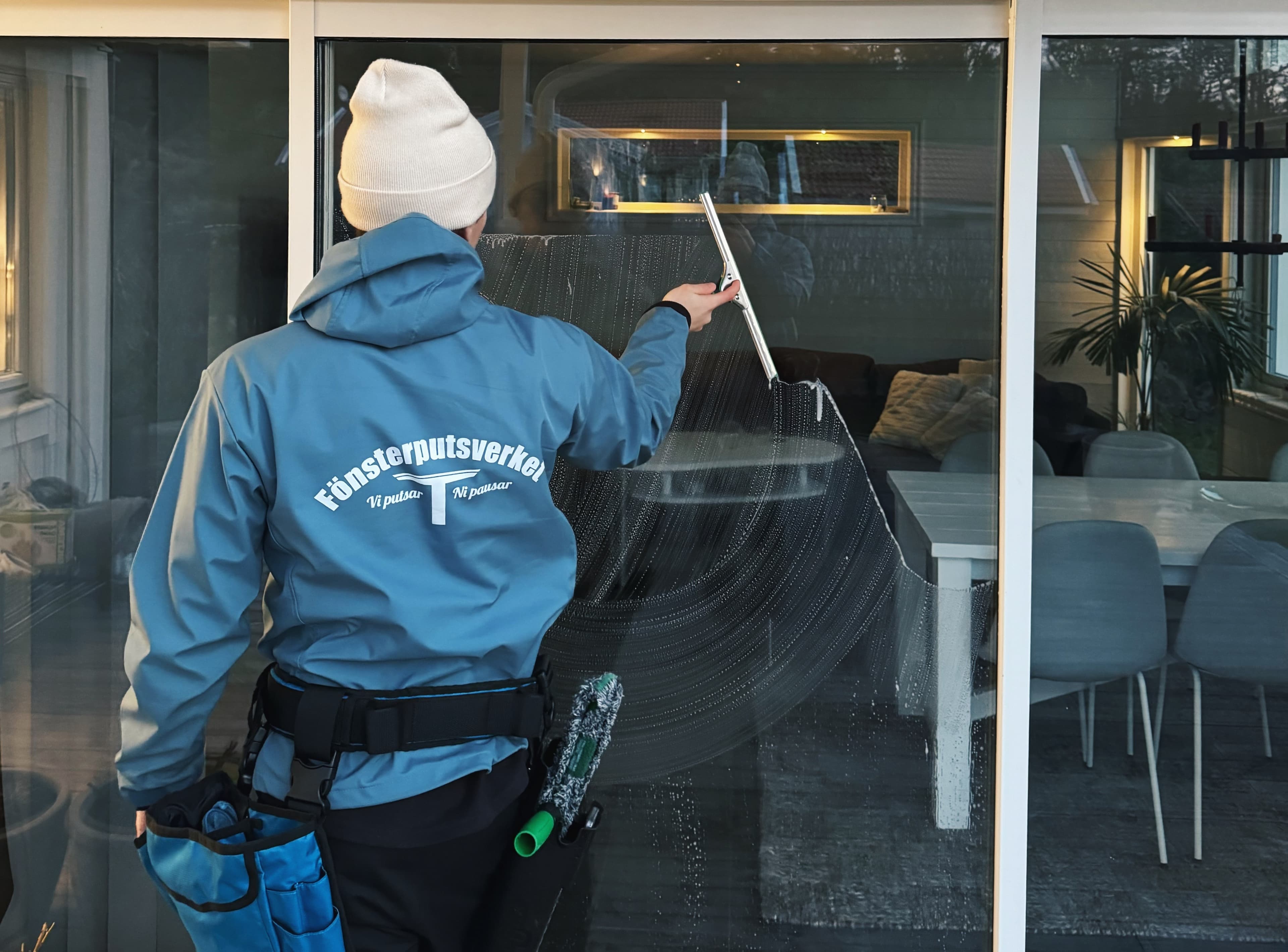 Fönsterputsare rengör ett glasparti med fönsterskrapa