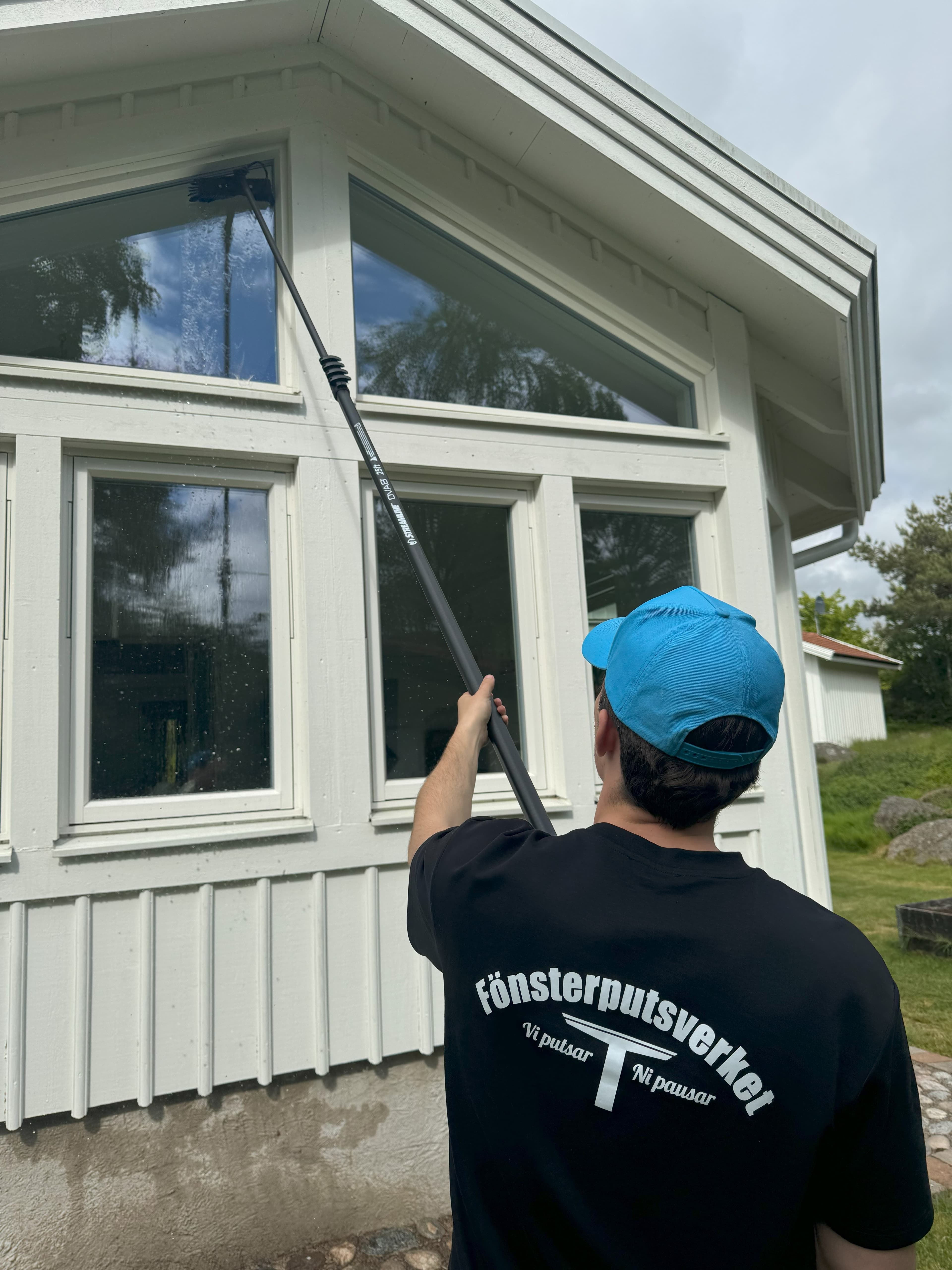 Fönsterputsare rengör ett högt gavelfönster med teleskopskaft